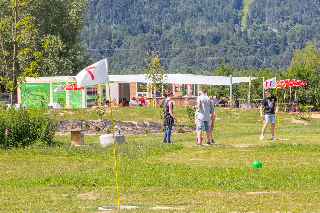 Eine Gruppe Erwachsener spielt Fußballgolf vor dem Kick2Gether-Bistro