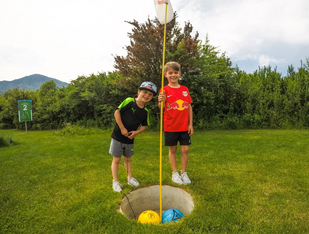 Zwei Kinder stehen mit gelbem und blauem Fußball am Ziel einer Fußballgolf-Bahn